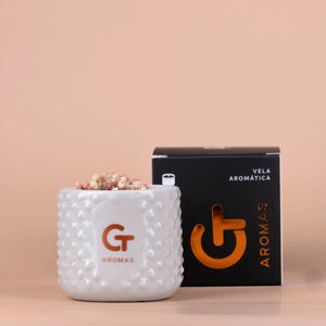 Vela aromática GT Aromas en vaso blanco texturizado y caja negra, fondo beige elegante.